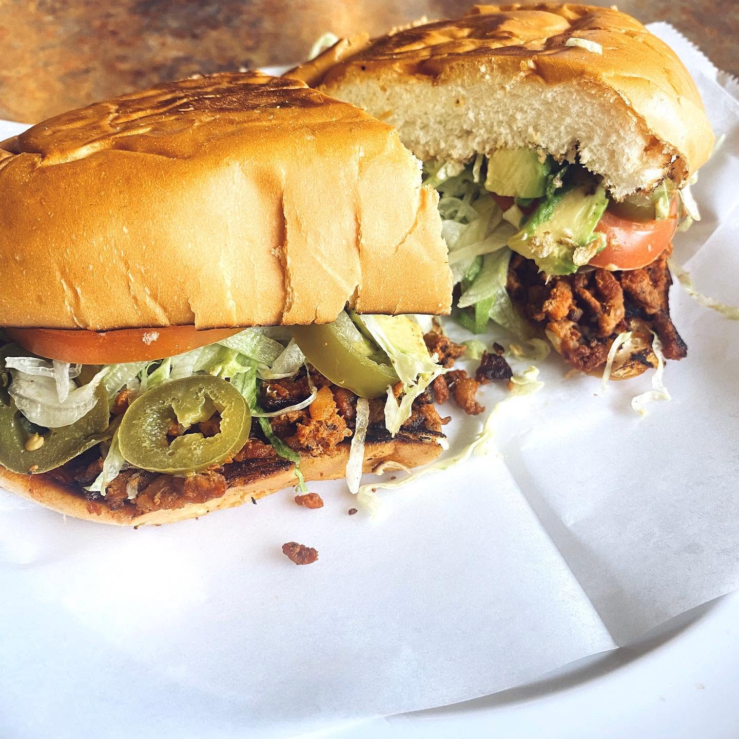 Torta al pastor on a toasted bolillo with lettuce, tomato, avocado, and pickled jalapeños.